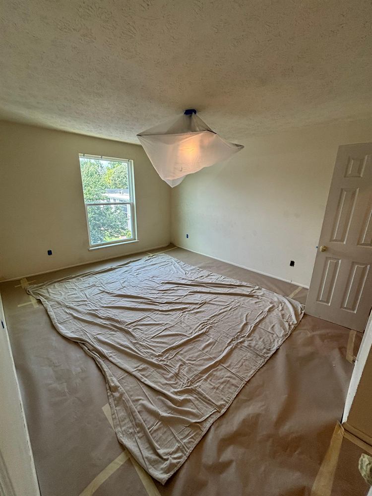 Room with covered floor and ceiling light fixture wrapped in plastic before painting