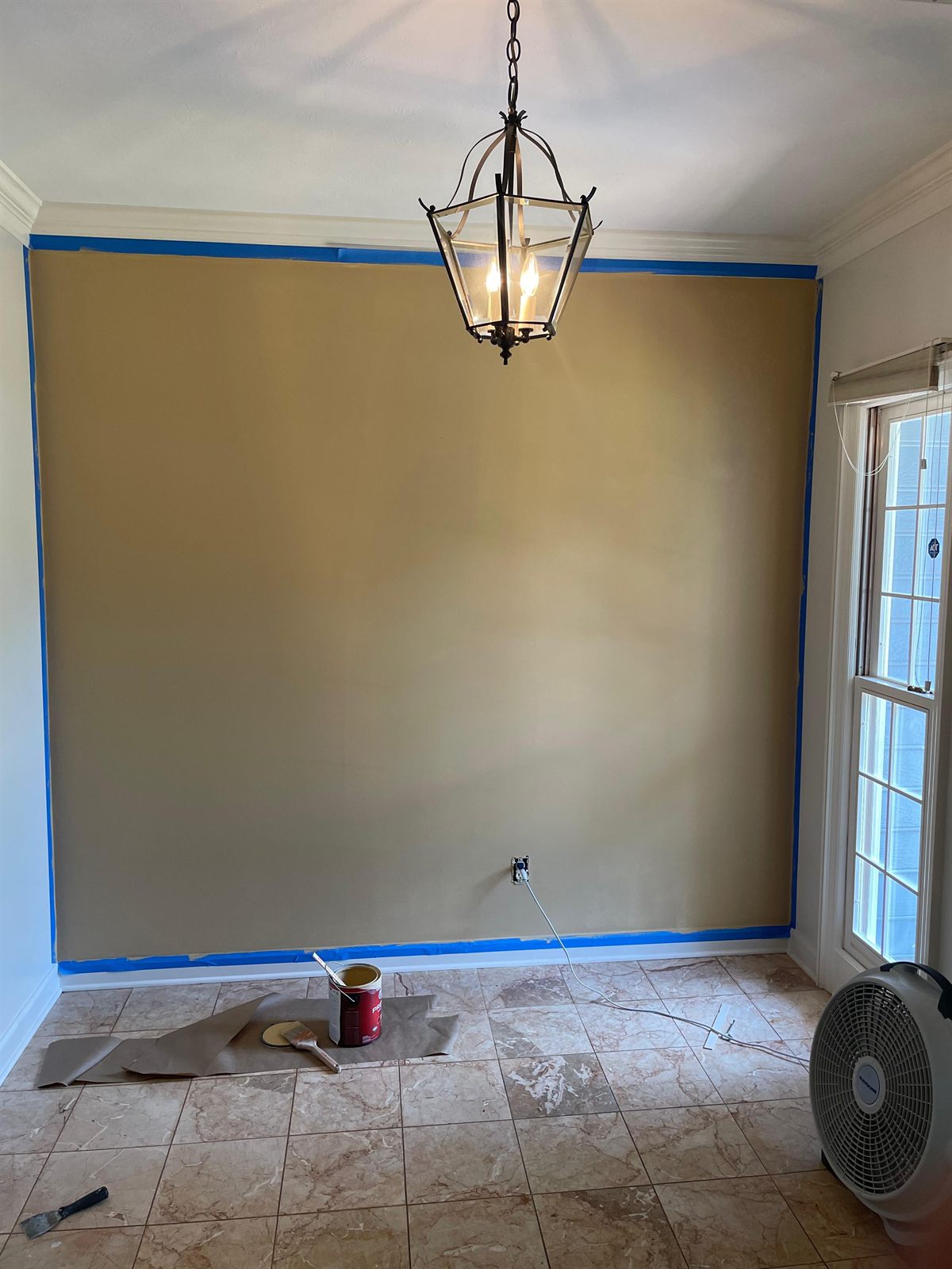 Wall masked with blue painter's tape along the ceiling, floor protected, before the finish coat